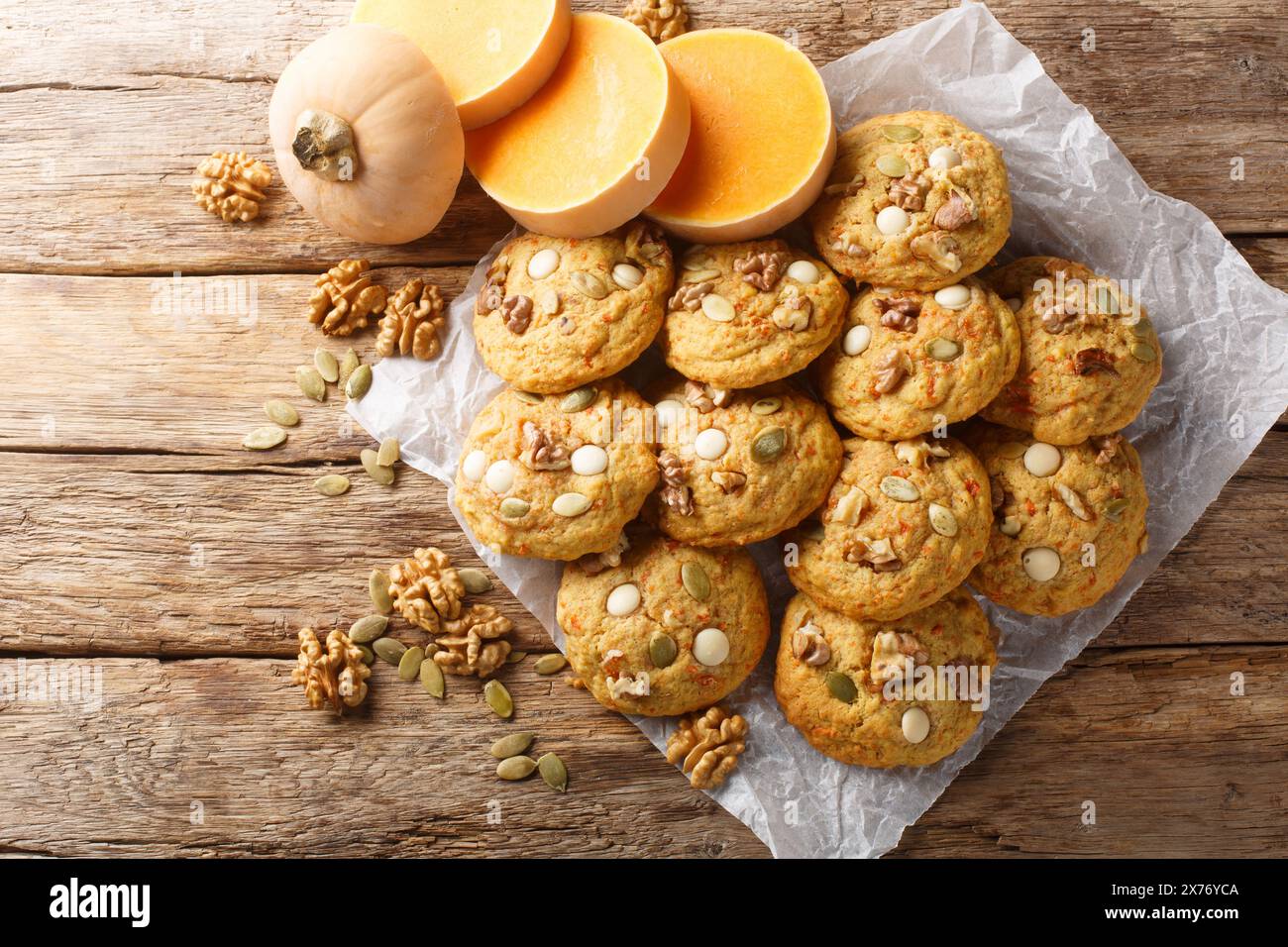 Biscuits à la citrouille sur Halloween avec des pépites de chocolat blanc, noix et graines de citrouille en gros plan sur le parchemin sur la table en bois. Vue horizontale de dessus fr Banque D'Images