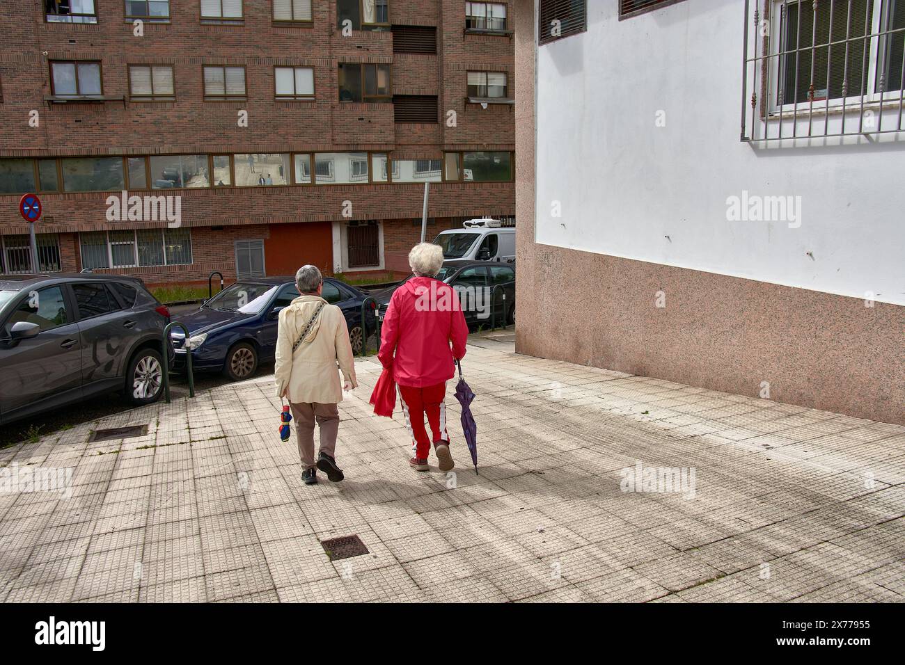 Deux femmes au dos méconnaissable marchent dans la rue en bavardant, l'une en survêtement rouge et l'autre en blanc ; elles ont toutes les deux les cheveux gris Banque D'Images