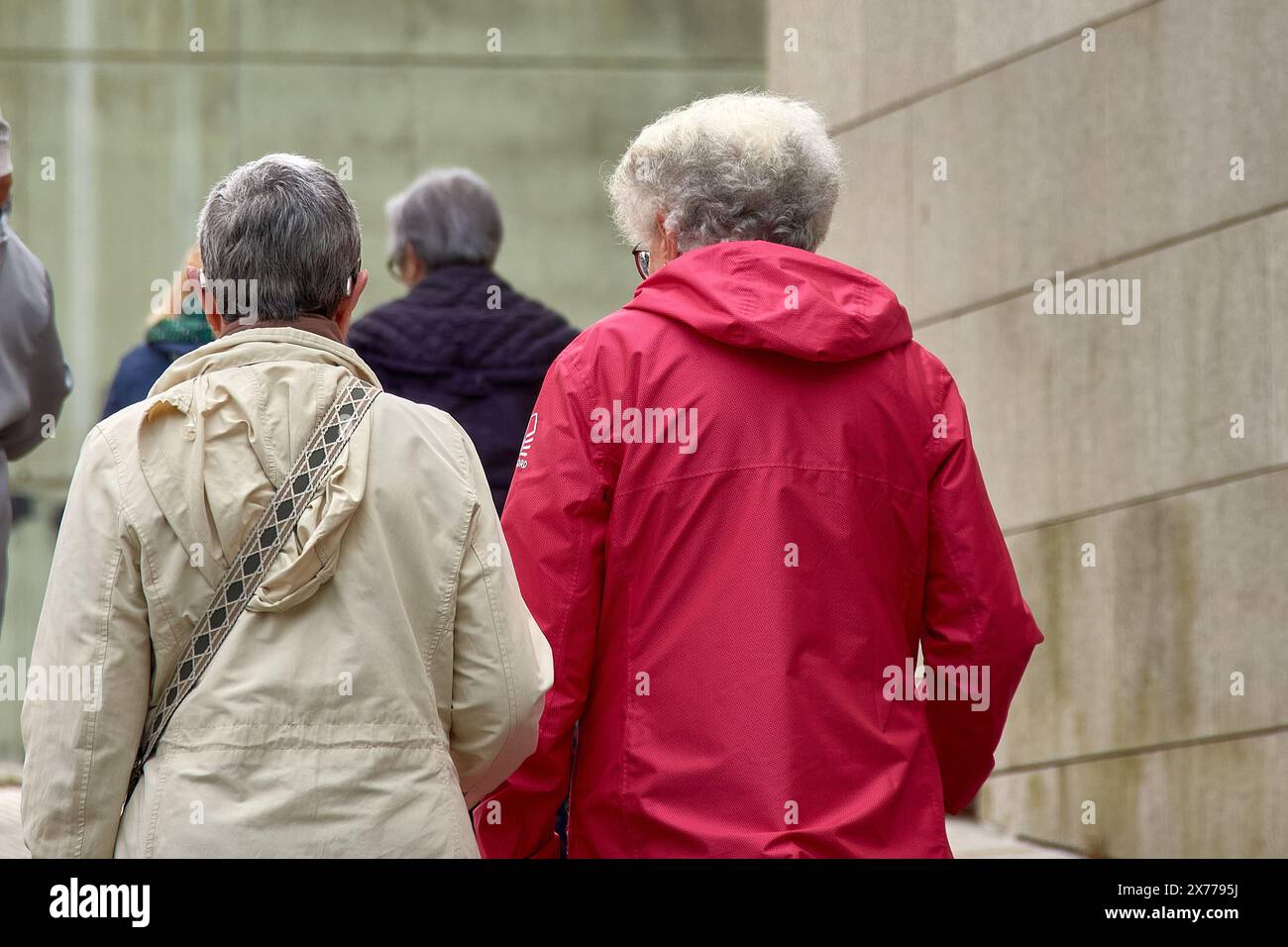 Deux femmes au dos méconnaissable marchent dans la rue en bavardant, l'une en survêtement rouge et l'autre en blanc ; elles ont toutes les deux les cheveux gris Banque D'Images