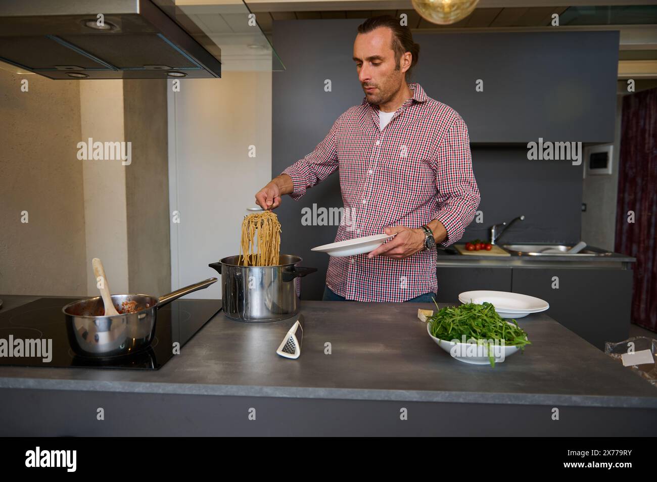 Beau jeune chef masculin versant le passé italien fraîchement cuit dans une assiette, prêt à servir aux clients. Consommation de nourriture et de boissons. Epicure. Cu Banque D'Images
