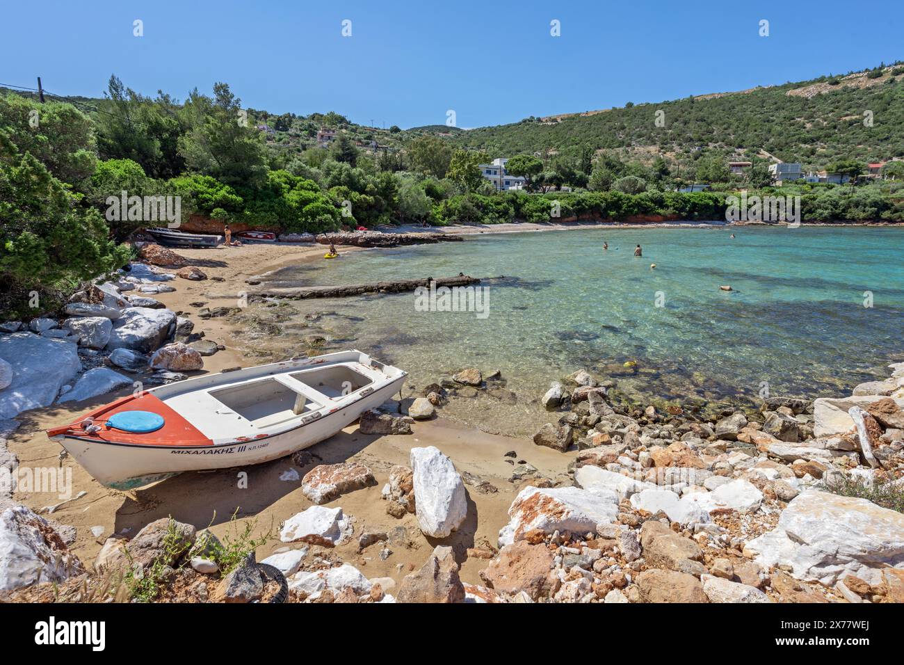 Plage d'Agia Marina avec un bateau traditionnel en bois et quelques personnes appréciant les eaux turquoises cristallines de cette plage de sable hors des sentiers battus. Banque D'Images