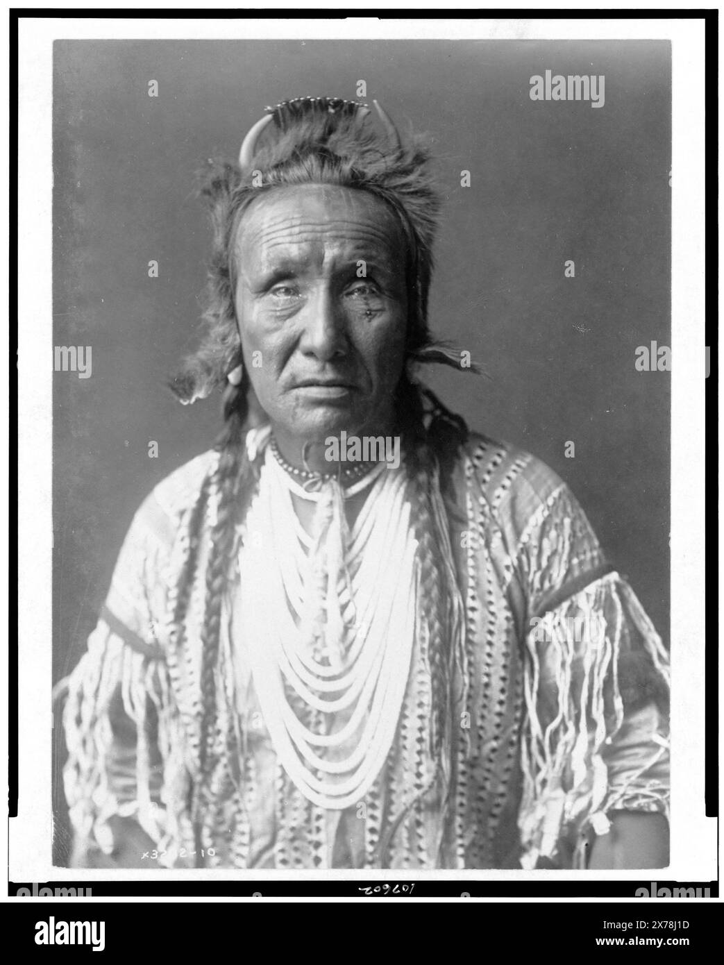 The Grizzly Bear, Piegan, portrait en demi-longueur, face avant, collection Edward S. Curtis., Curtis no. 3232-10., publié dans : The North American Indian / Edward S. Curtis. [Seattle, Washington] : Edward S. Curtis, 1907-30, v. 6, p. 20.. Indiens d'Amérique du Nord, vêtements et robes, 1910. , Indiens Piegan, vêtements et robes, 1910. Banque D'Images