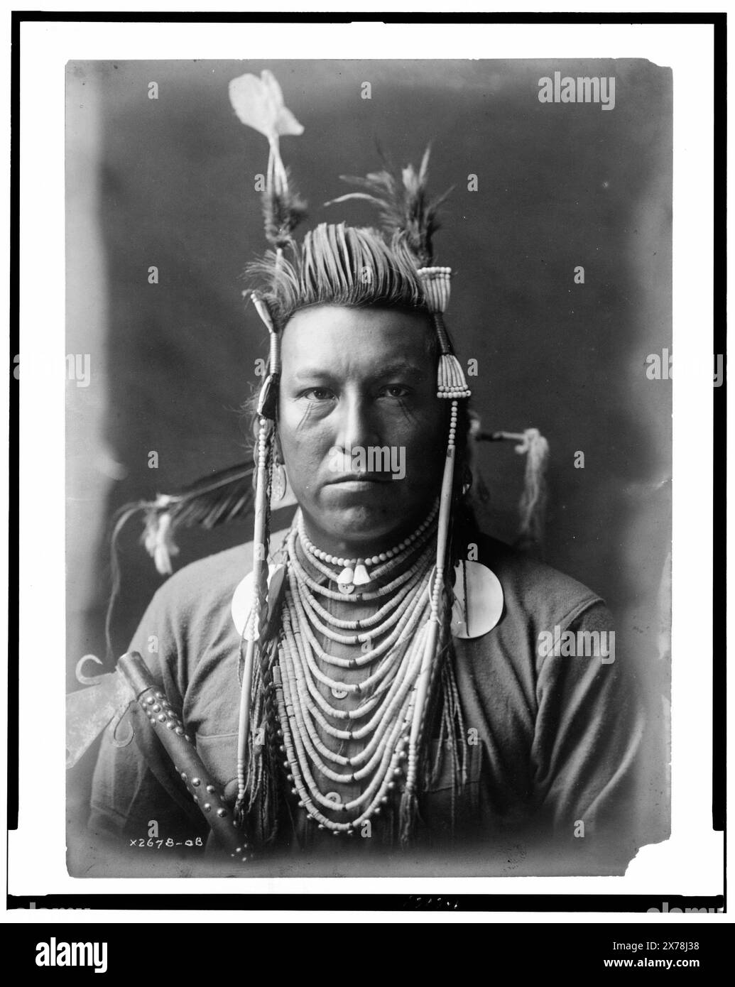Avalez oiseau, Crow Indian, Montana, portrait de la tête et des épaules, face avant, pompadour peint, coiffe Apsaroke, chemise en flanelle, perles sur la poitrine, pipe cloutée tenue devant le bras droit, collection Edward S. Curtis., Curtis no. 2678-08.. Avalez oiseau. , Indiens d'Amérique du Nord, Montana, vêtements et robes, 1900-1910. , Crow Indians, vêtements et robes, 1900-1910. Banque D'Images