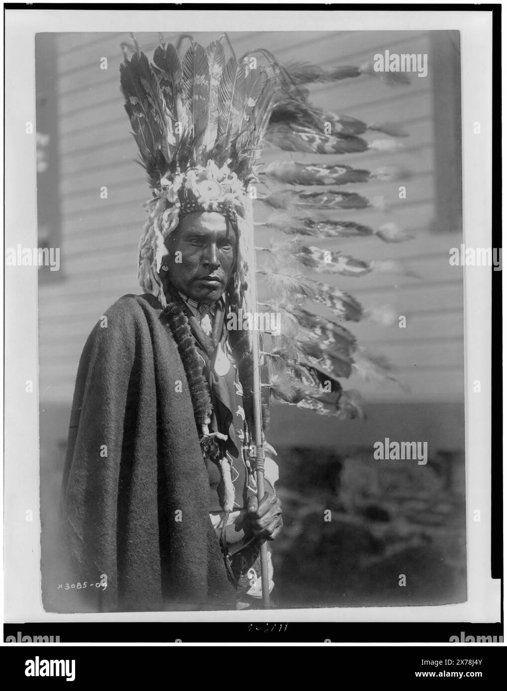 Piegan War-bonnet et coup-stick, au verso de la photographie : Dan Bull Plume ; sur l'étiquette du dossier : Rueben Black Boy., Edward S. Curtis Collection ., Curtis no. 3085-09., publié dans : The North American Indian / Edward S. Curtis. [Seattle, Washington] : Edward S. Curtis, 1907-30, v. 6, p. 16.. Indiens d'Amérique du Nord, vêtements et robes, 1910. , Indiens Piegan, vêtements et robes, 1910. Banque D'Images