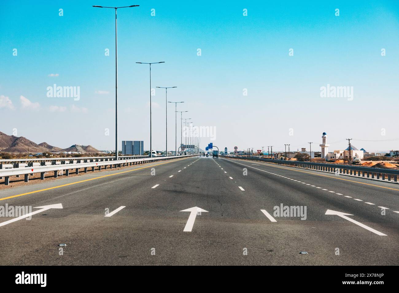 Autoroute moderne et vide à Oman avec des panneaux de limitation de vitesse, des lampadaires et un ciel bleu clair, montrant l'infrastructure routière et les transports Banque D'Images