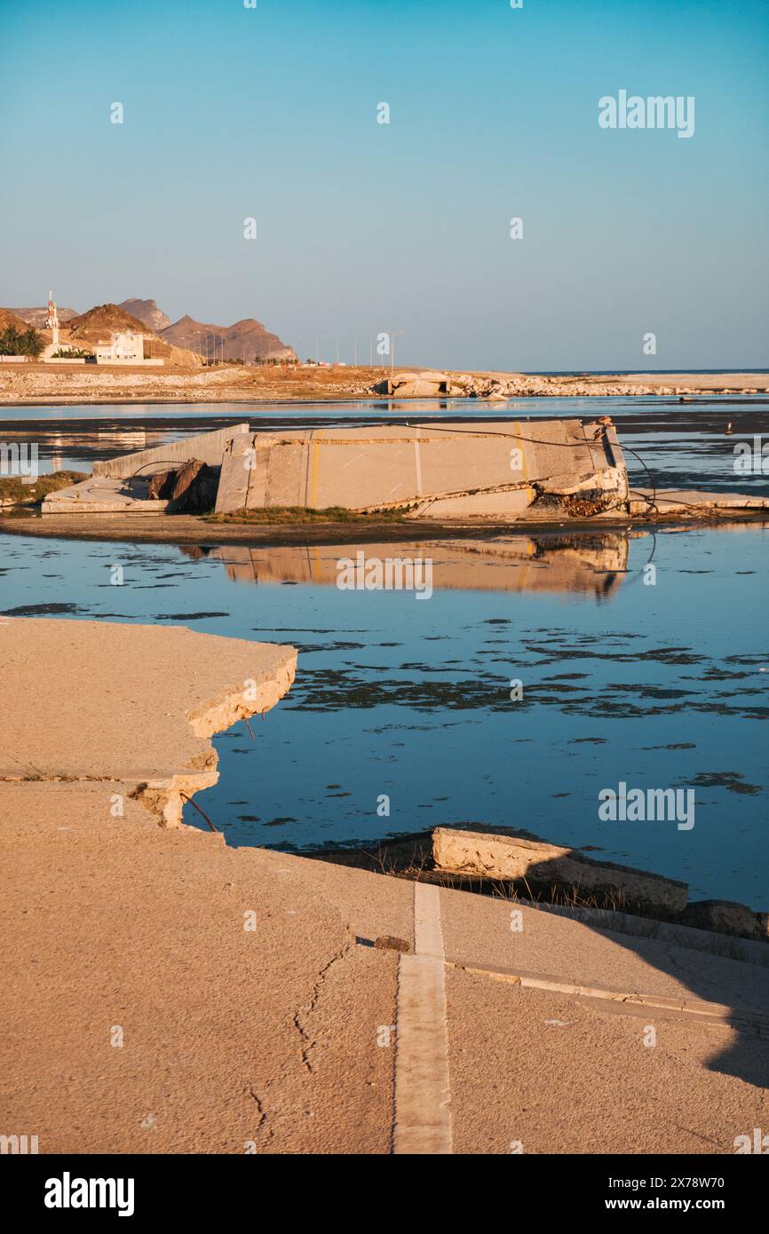 Pont effondré à Al Mughsail Beach à Oman, avec des tronçons de route brisés menant à l'eau peu profonde contre une montagne côtière en toile de fond. Banque D'Images