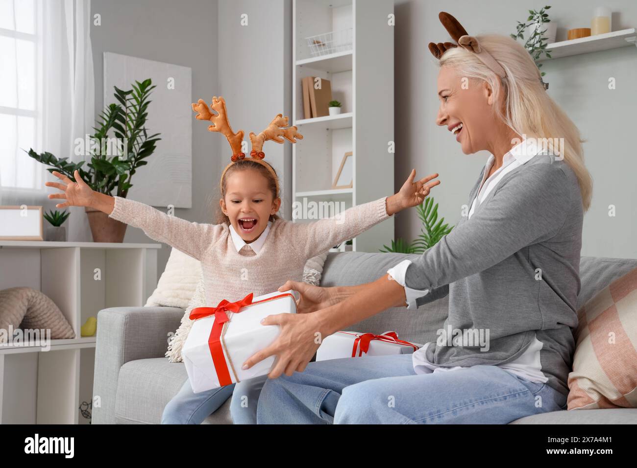 Petite fille et sa grand-mère en cornes de renne avec des cadeaux à la maison la veille de Noël Banque D'Images