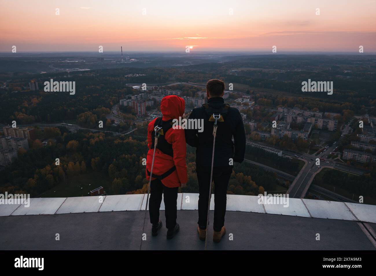 Un couple admire la vue sur le coucher du soleil, attaché par câble et harnais à la plate-forme d'observation extérieure de la tour de télévision de Vilnius, en Lituanie Banque D'Images
