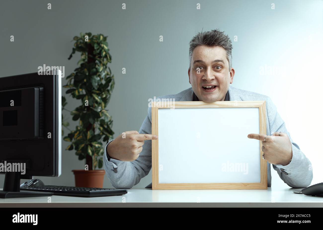 homme en costume léger et cravate rayée, souriant largement, pointe vers un tableau blanc vierge. Son expression enthousiaste suggère qu'il est désireux de présenter ou de comm Banque D'Images