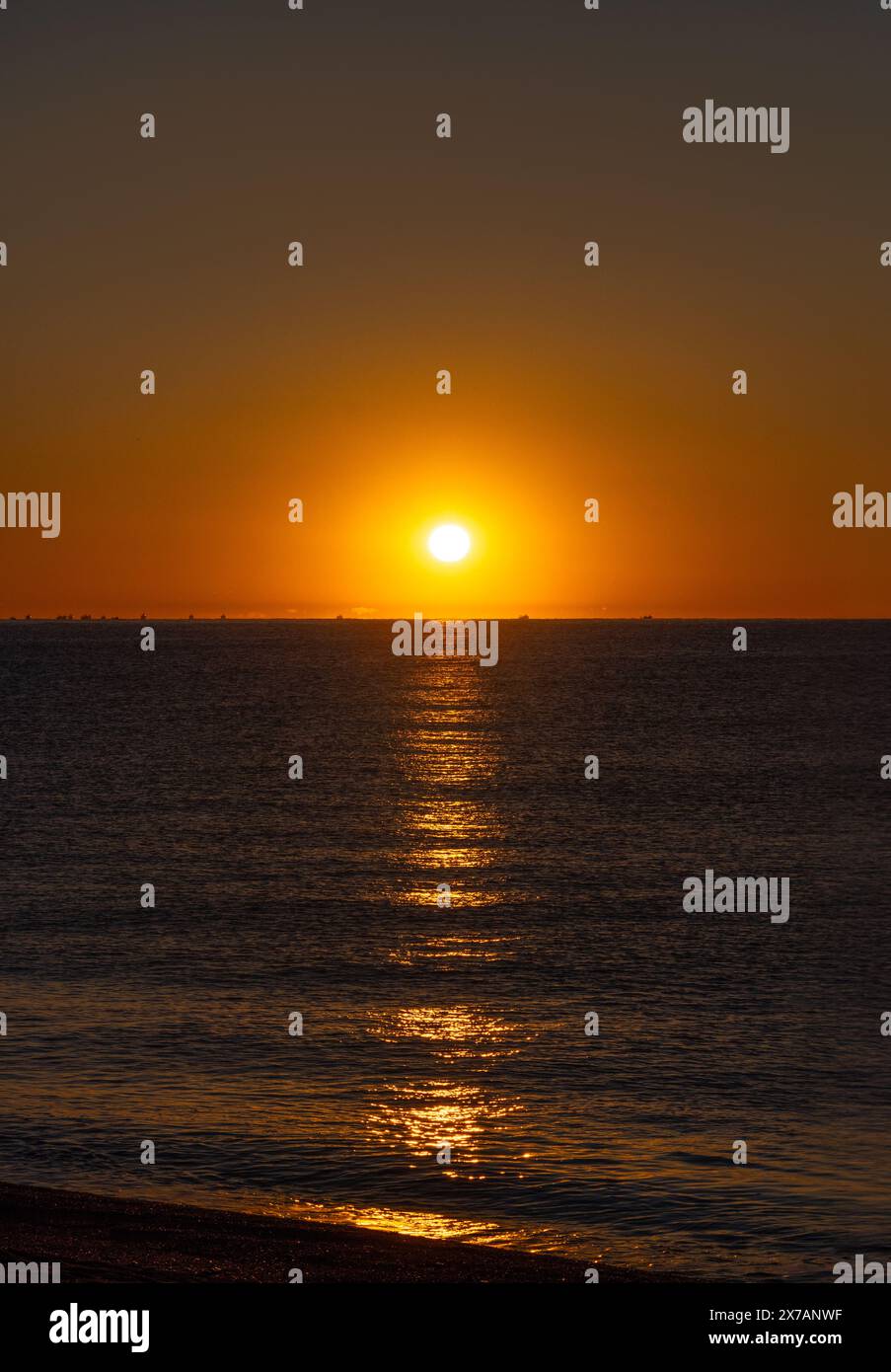 Mer calme illuminée par la lumière orange du soleil de l'aube illuminant les silhouettes d'un groupe de bateaux de pêche pêchant la crevette Palamos Banque D'Images