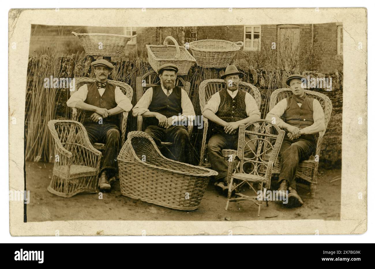 Carte postale originale de l'ère édouardienne de 4 fabricants de paniers de saule et de chaises, un peut-être un apprenti peut-être les niveaux Somerset, Norfolk ou Suffolk. Certains personnages, affichant fièrement leurs vêtements de basket et leurs meubles. Willow Wiies empilés dans le fond, les ouvriers édouardiens. Circa 1910, Royaume-Uni Banque D'Images