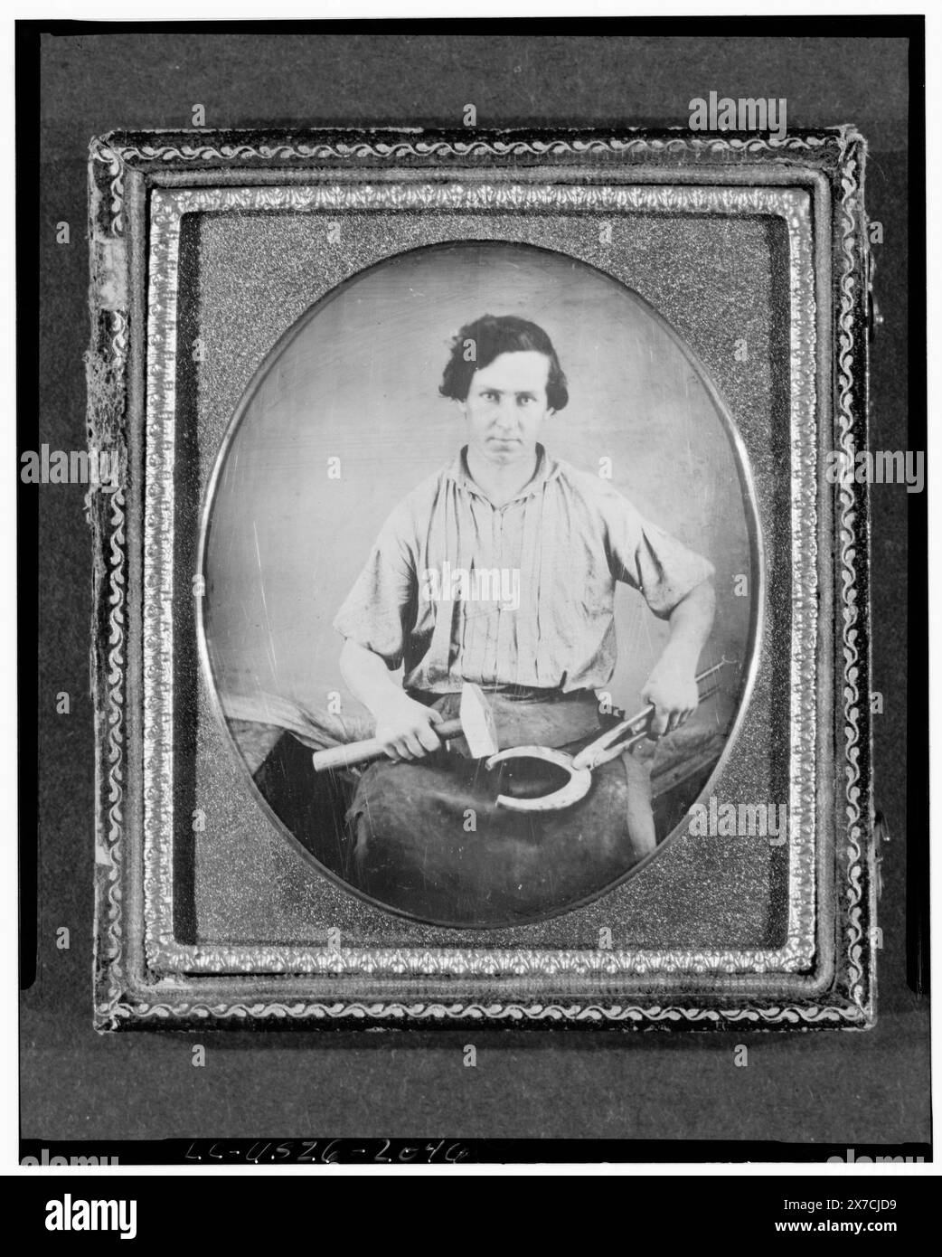 Portrait professionnel d'un forgeron, de trois quarts de long, face à l'avant, tenant un fer à cheval avec une pince dans une main et un marteau dans l'autre, photographe non identifié., Hallmark : Rinhart 29., cas : arrière seulement, dessin quadrifeuille avec bordure géométrique entrelacée., achat/échange ; Gary Vroegindewey ; 1981 ; (DLC/PP-1981:380R.15)., fait partie de : collection daguerréotype Blacksmiths, 1850-1860. Banque D'Images