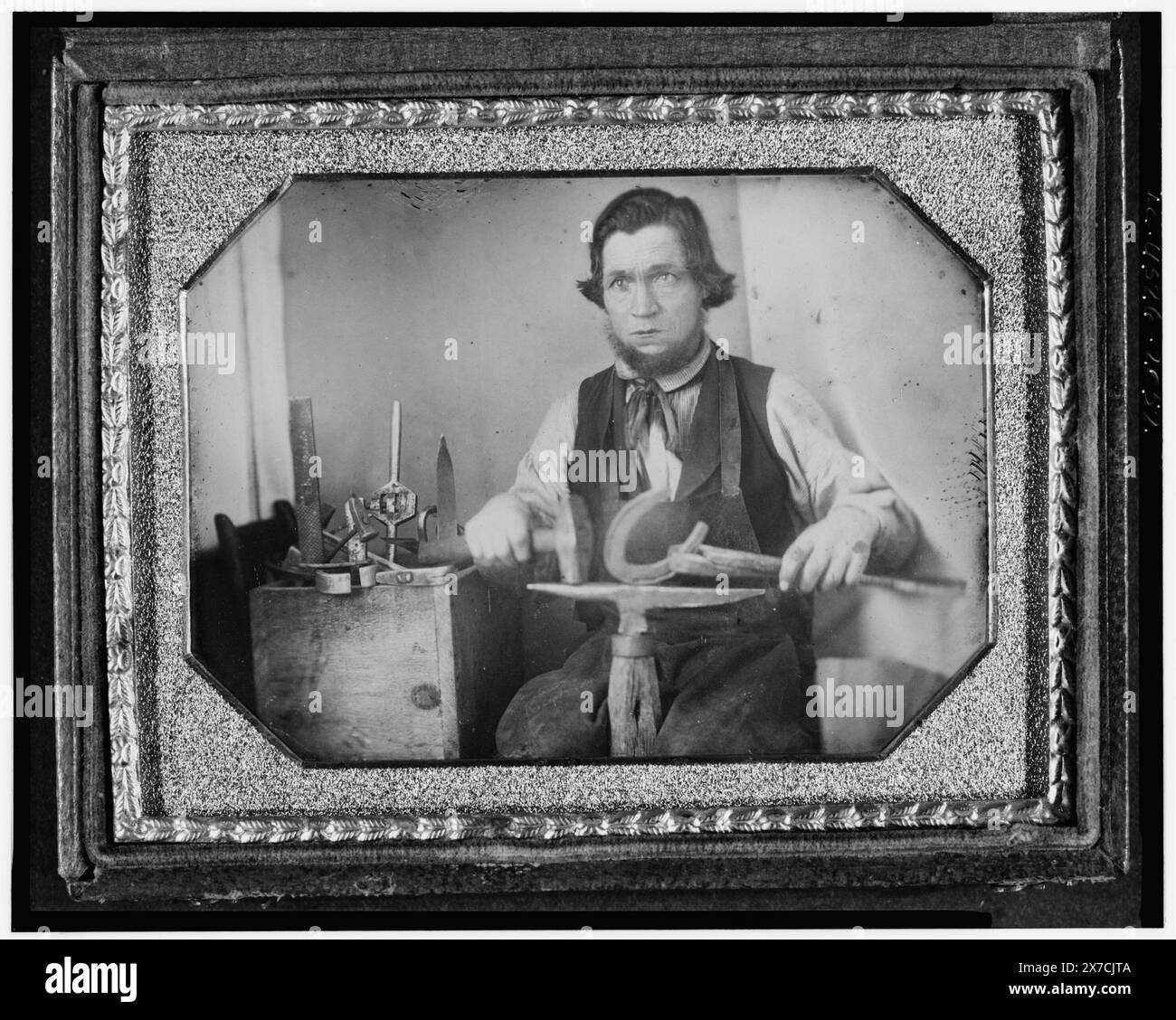 Portrait professionnel d'un forgeron, de trois quarts de longueur, travaillant sur un fer à cheval à une enclume, d'autres outils à son côté, photographe non identifié., Hallmark : [deux oiseaux sur un arbre] 40., cas : Rinhart 131., carte de visite d'accompagnement : H.F. Kirlin, Carpenter & Builder, No. 916 South Seventh Below Christian, Philadelphie. Travail [main] rapidement pris en charge. Evans' Fast Press., achat/échange ; Gary Vroegindewey ; 1981 ; (DLC/PP-1981:380R.20)., fait partie de : collection daguerréotype Blacksmiths, 1840-1860. Banque D'Images