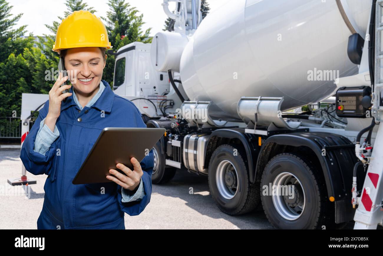 Travailleuse avec tablette numérique à côté de la pompe à béton montée sur camion avec mélangeur. Banque D'Images