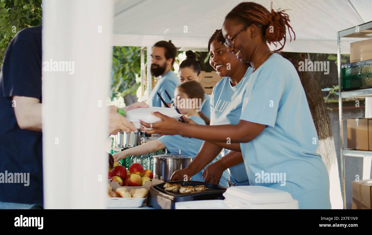 De généreux volontaires portant des t-shirts bleus donnent des repas gratuits et une aide humanitaire à ceux qui en ont besoin. Les pauvres et les sans-abri de toutes races sont nourris par l'organisation à but non lucratif. Vue latérale, portable. Banque D'Images