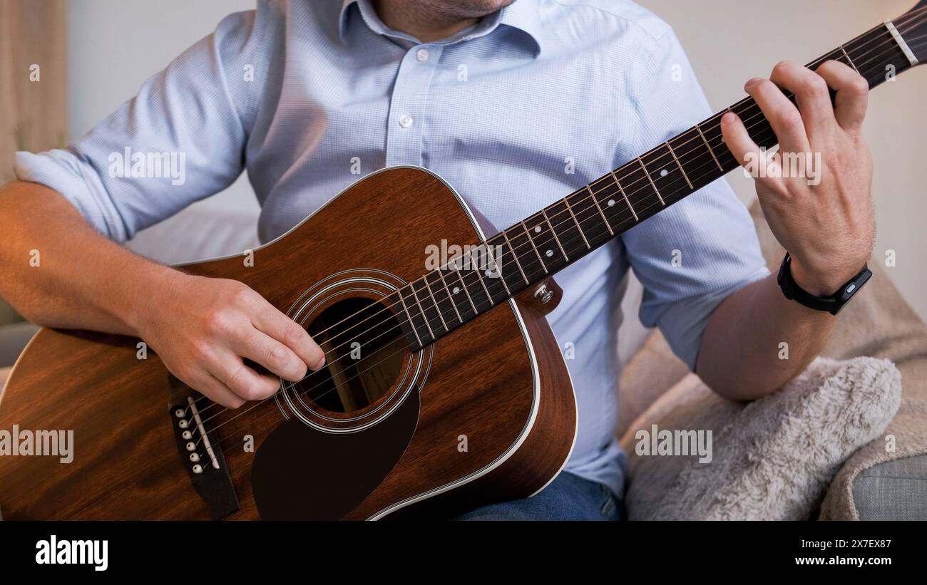 Habileté à la guitare. Pratique musicale. Homme occasionnel étudiant assis sur le canapé apprenant les mains jouant la mélodie de l'instrument à cordes dans l'intérieur du salon à la maison. Banque D'Images