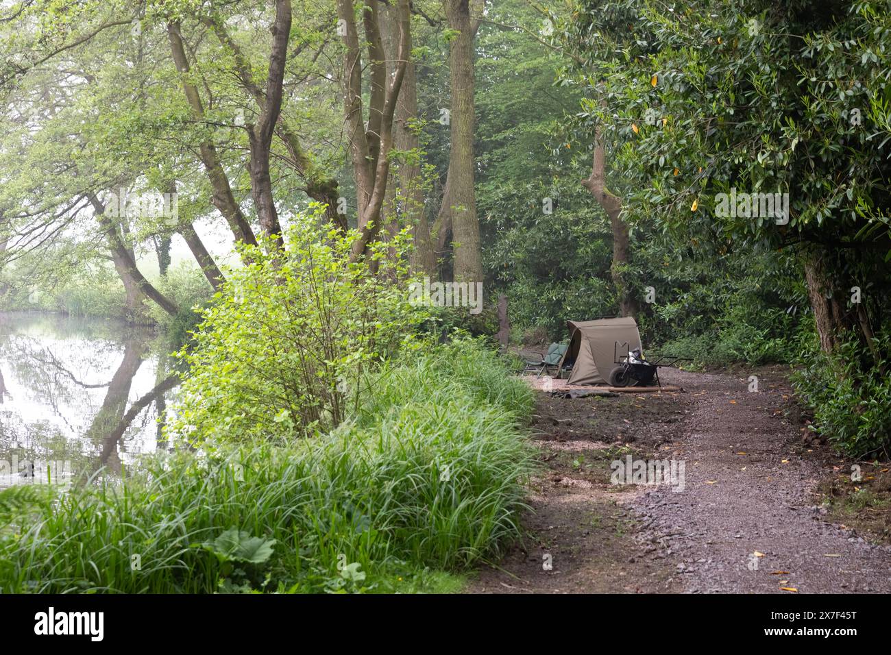 Regardant en bas d'un sentier au bord d'une piscine une mise en place de pêche. Un bivvy est planté au bord de la piscine avec brouette et chaise. Pas de personnes et d'espace texte Banque D'Images