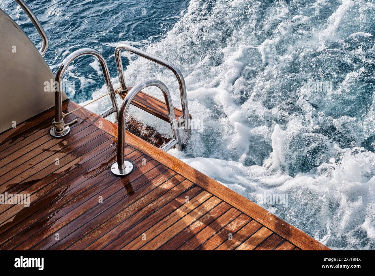 Pont arrière en bois de teck et échelle métallique d'un yacht à moteur, vagues et éclaboussures de mer et mousse. Banque D'Images