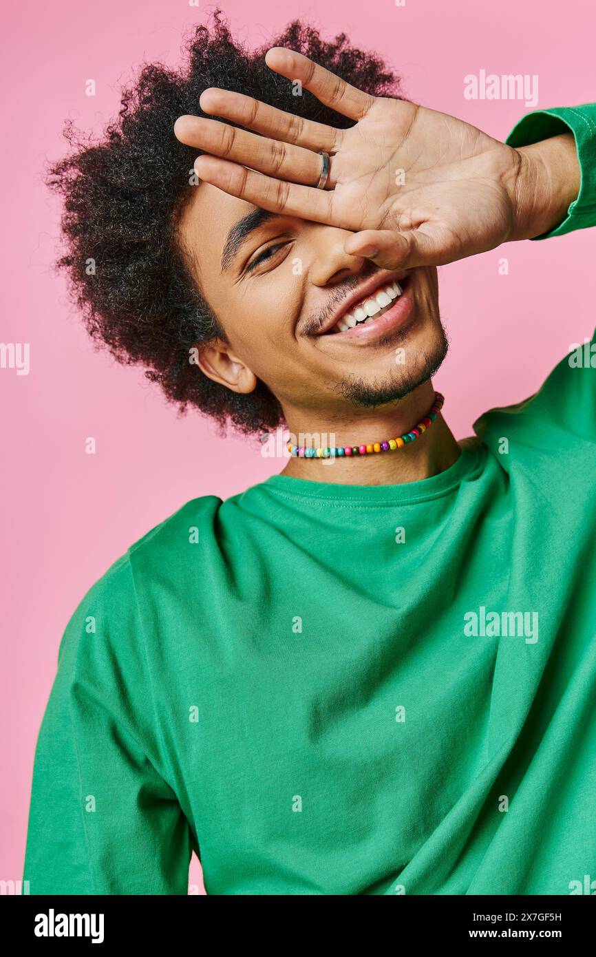 Un jeune homme afro-américain joyeux dans une chemise verte, tenant sa main sur son visage, montrant un geste émotionnel. Banque D'Images