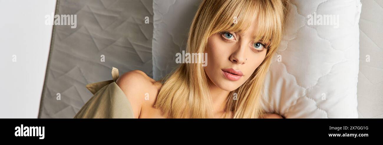 Une femme blonde dans une tenue confortable se trouve paisiblement sur un lit. Banque D'Images