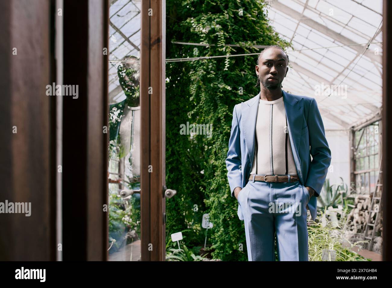 Homme afro-américain sophistiqué en costume pose dans une serre vibrante. Banque D'Images
