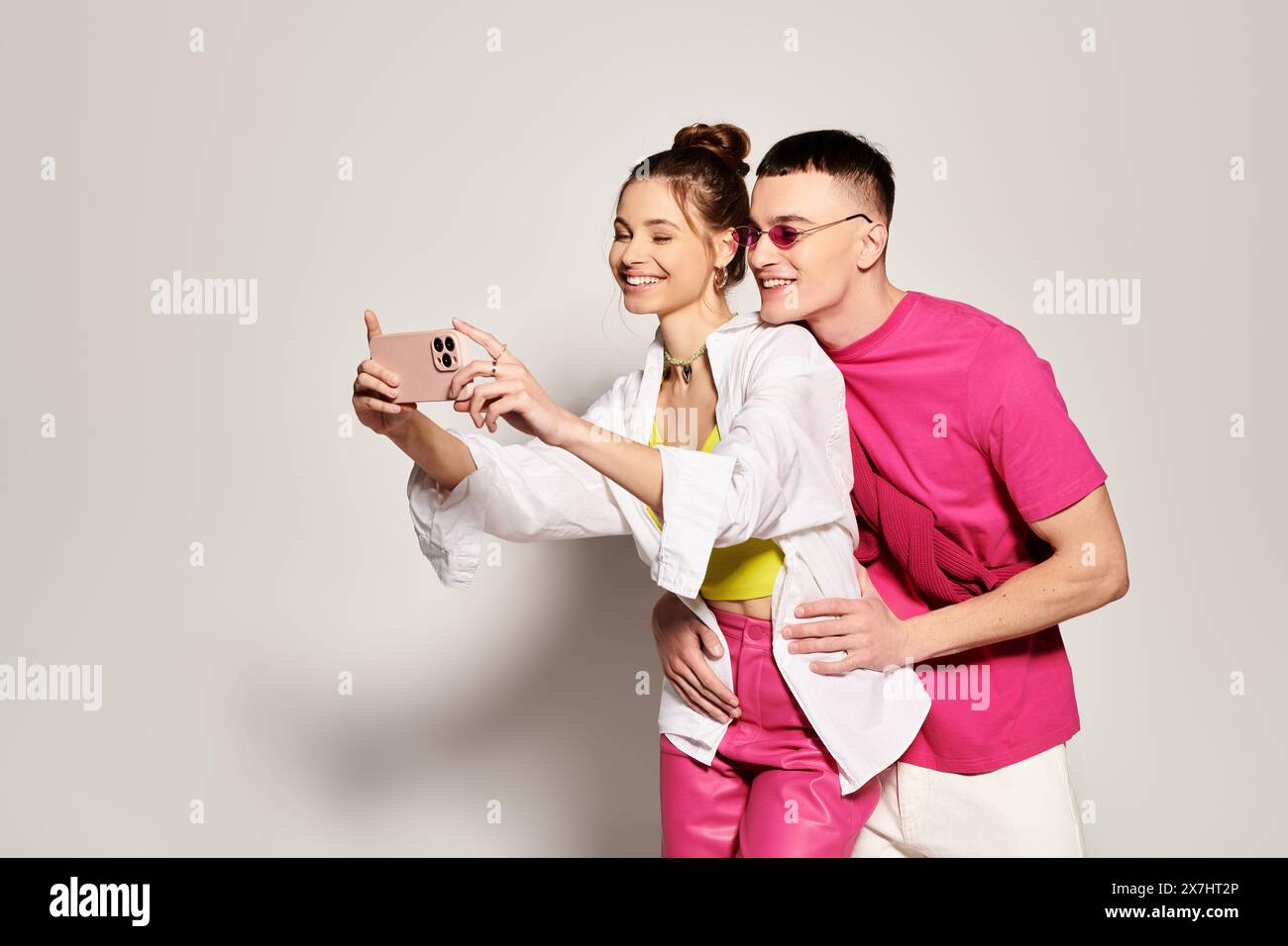 Jeune couple élégant sourit tout en prenant un selfie avec un téléphone portable dans un studio sur un fond gris. Banque D'Images