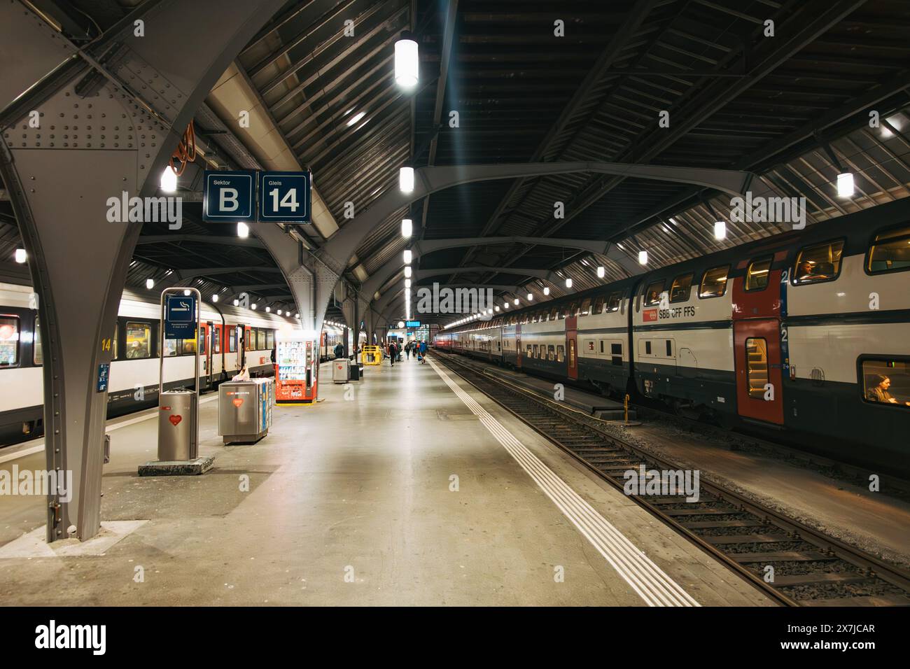Un quai de train déserté dans la gare centrale de Zurich, éclairé par des plafonniers, avec des trains CFF en attente à d'autres quais Banque D'Images