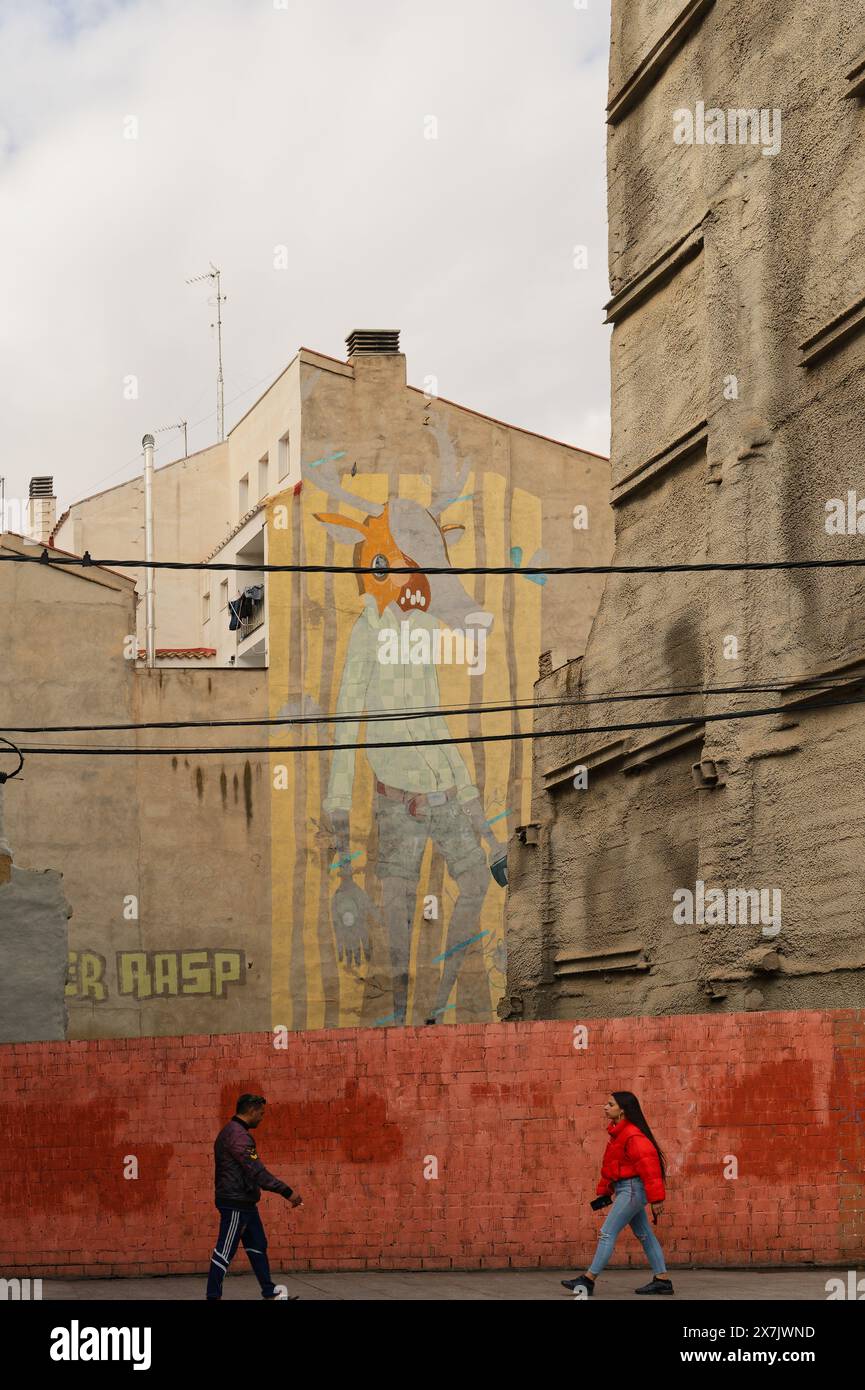 Une murale fantaisiste anime le paysage urbain silencieux de Saragosse, contrastant avec les murs Unis, tandis que deux personnes dans des directions opposées s'approchent l'une de l'autre. Banque D'Images