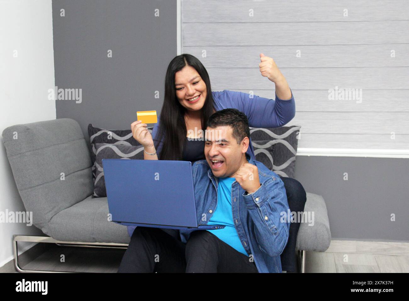 Couple d'un homme et d'une femme latino de 40 ans utilisent leur ordinateur portable et leur carte de crédit pour magasiner en ligne excités par les réductions et les promotions Banque D'Images