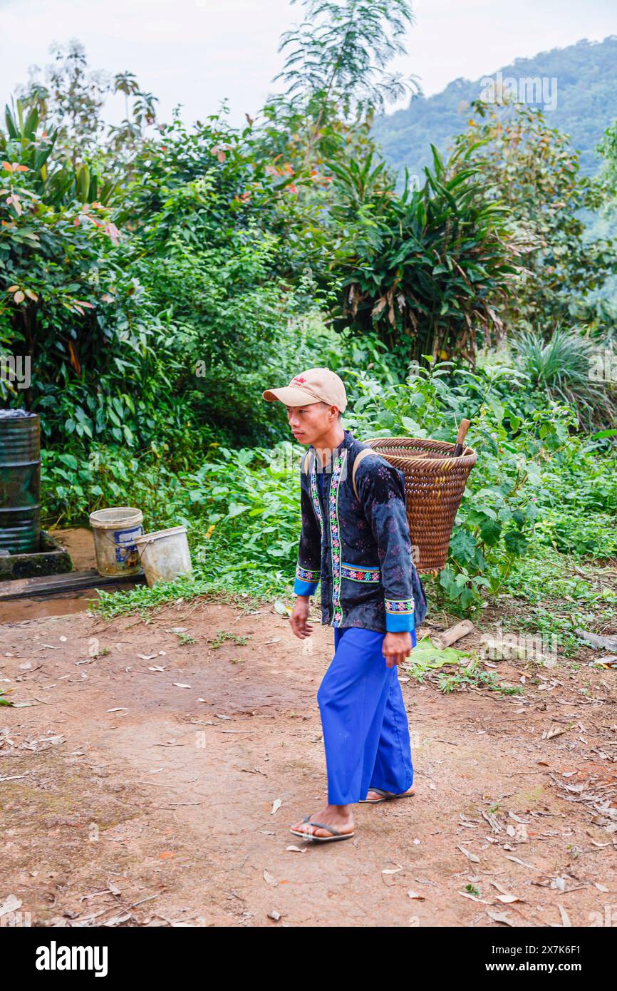 Un jeune homme portant un panier en osier habillé dans des vêtements typiques de paj ntaub ou de tissu de fleurs Hmong, Chiang Khong, province de Chiang Rai, nord de la Thaïlande Banque D'Images