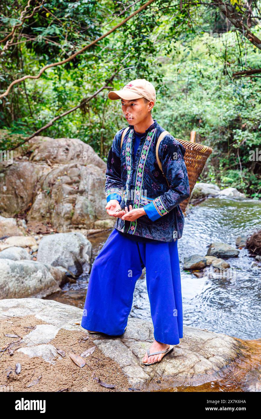 Un jeune homme portant un panier en osier habillé dans des vêtements typiques de paj ntaub ou de tissu de fleurs Hmong, Chiang Khong, province de Chiang Rai, nord de la Thaïlande Banque D'Images