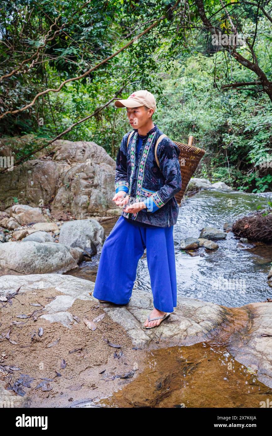 Un jeune homme portant un panier en osier habillé dans des vêtements typiques de paj ntaub ou de tissu de fleurs Hmong, Chiang Khong, province de Chiang Rai, nord de la Thaïlande Banque D'Images