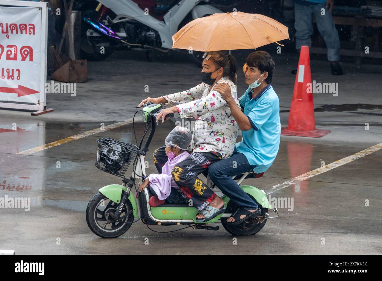 SAMUT PRAKAN, THAÏLANDE, 20 mars 2024, Une famille avec des parapluies monter un vélo électrique sous la pluie Banque D'Images