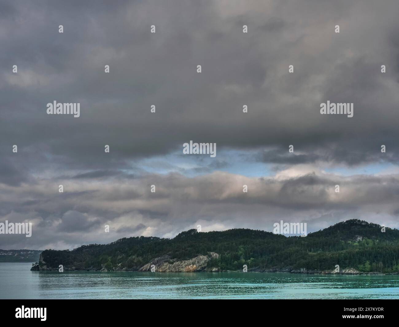 Nature photo d'un lac, flanqué de forêt et de montagnes, sous un ciel gris, nuageux, une eau chatoyante verdâtre dans un fjord aux sommets enneigés et Banque D'Images