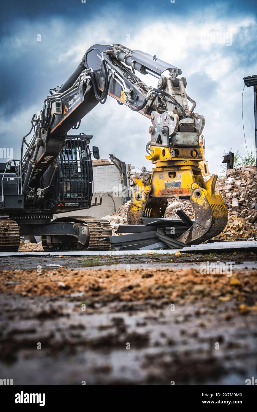 Une pelle avec des outils jaune vif travaille sur un chantier de construction boueux, entouré de débris sous un ciel gris, démolition, Saarbruecken, Allemagne Banque D'Images