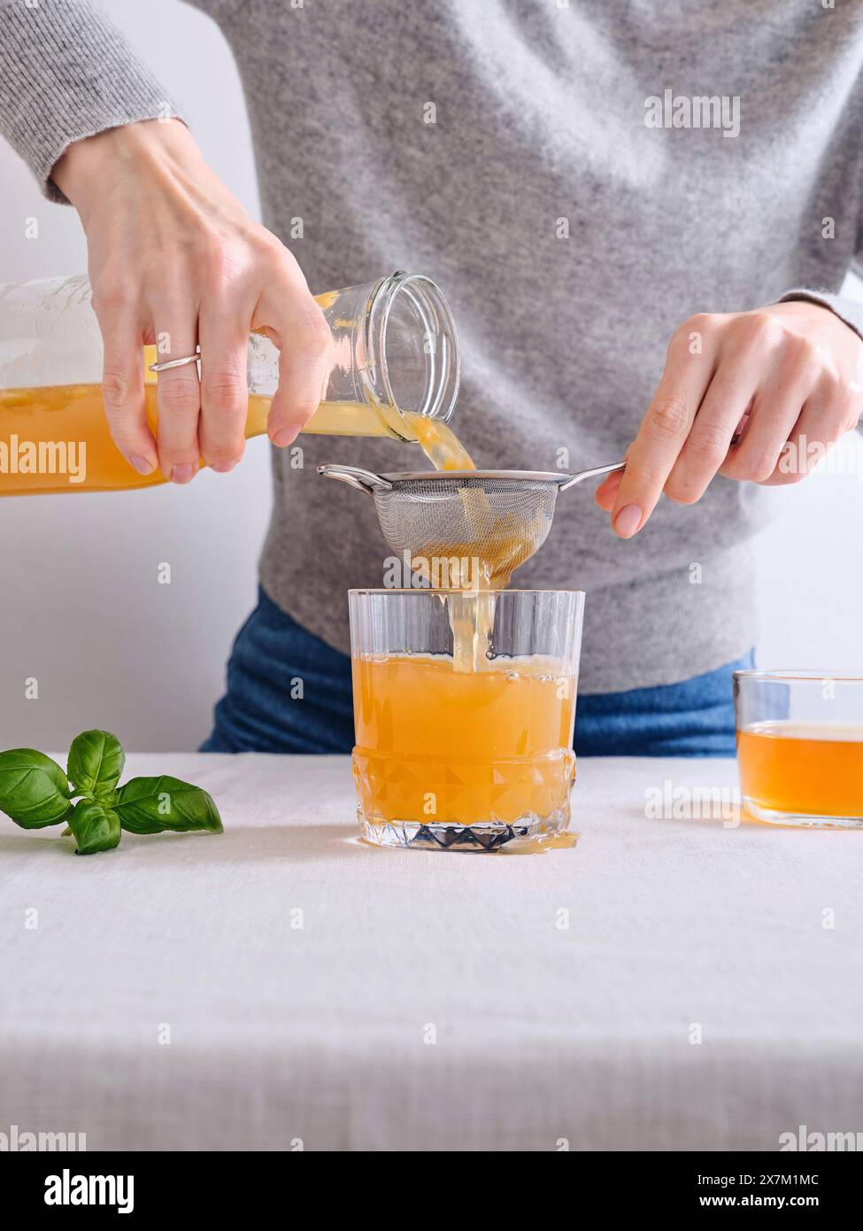Modèle féminin versant du komucha bio fait maison d'une bouteille dans un verre debout sur fond blanc Banque D'Images