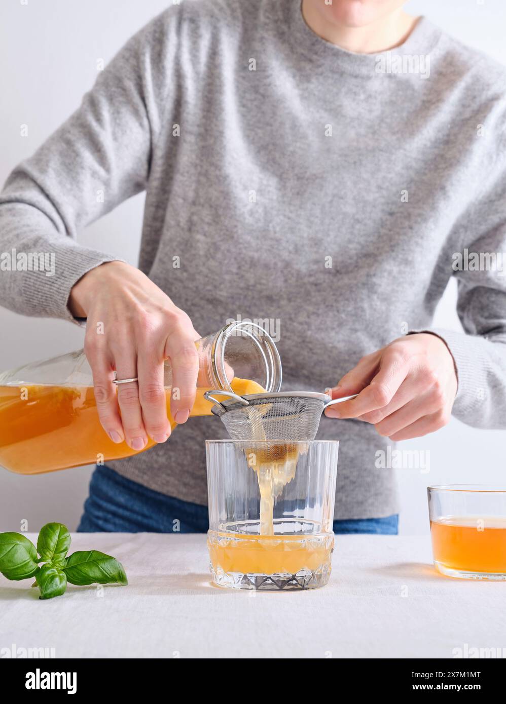 Modèle féminin versant du komucha bio fait maison d'une bouteille dans un verre debout sur fond blanc Banque D'Images