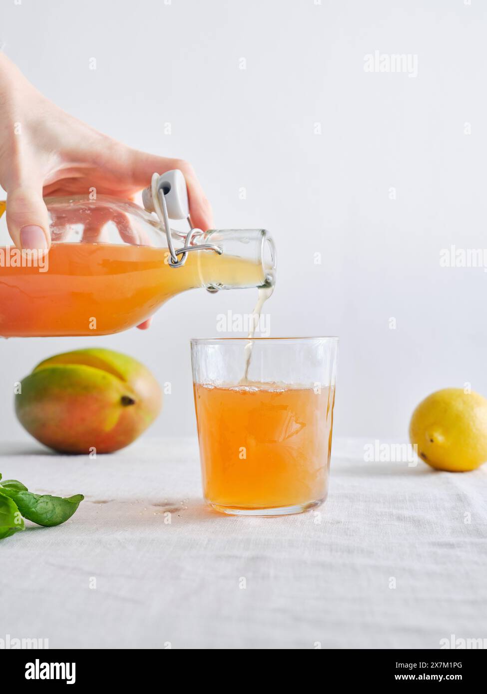 Main femelle versant de la limonade kombucha fermentée maison bio d'une bouteille dans un verre Banque D'Images