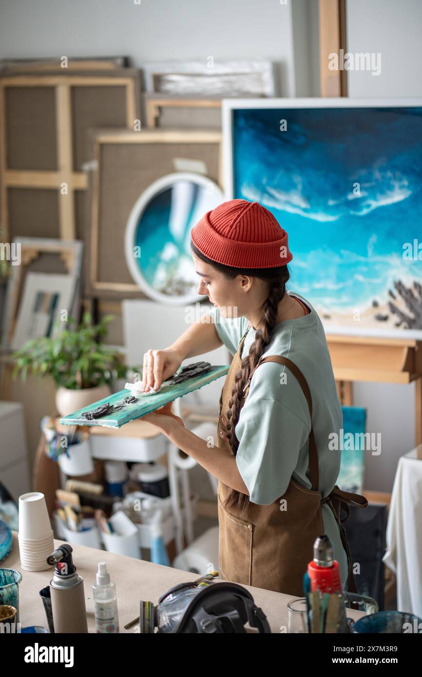 L'artiste féminine créative focalisée travaille sur les touches de finition des œuvres d'art en résine époxy dans le studio d'artisanat d'art Banque D'Images