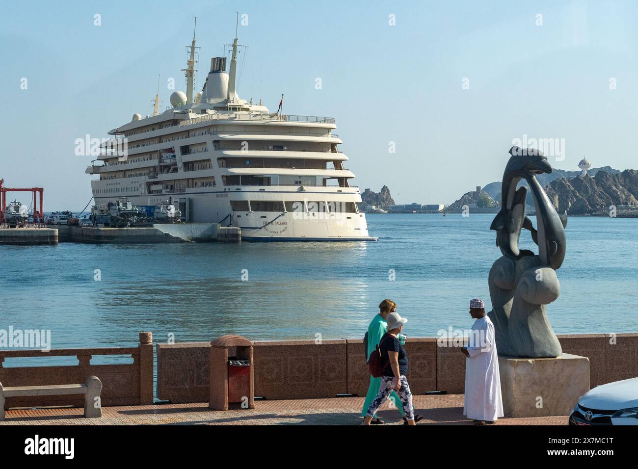 Muscat, Oman - 2 janvier 2024 : un résident local en tenue traditionnelle et un touriste en tenue occidentale passent devant une sculpture d'art moderne sur la mer Banque D'Images