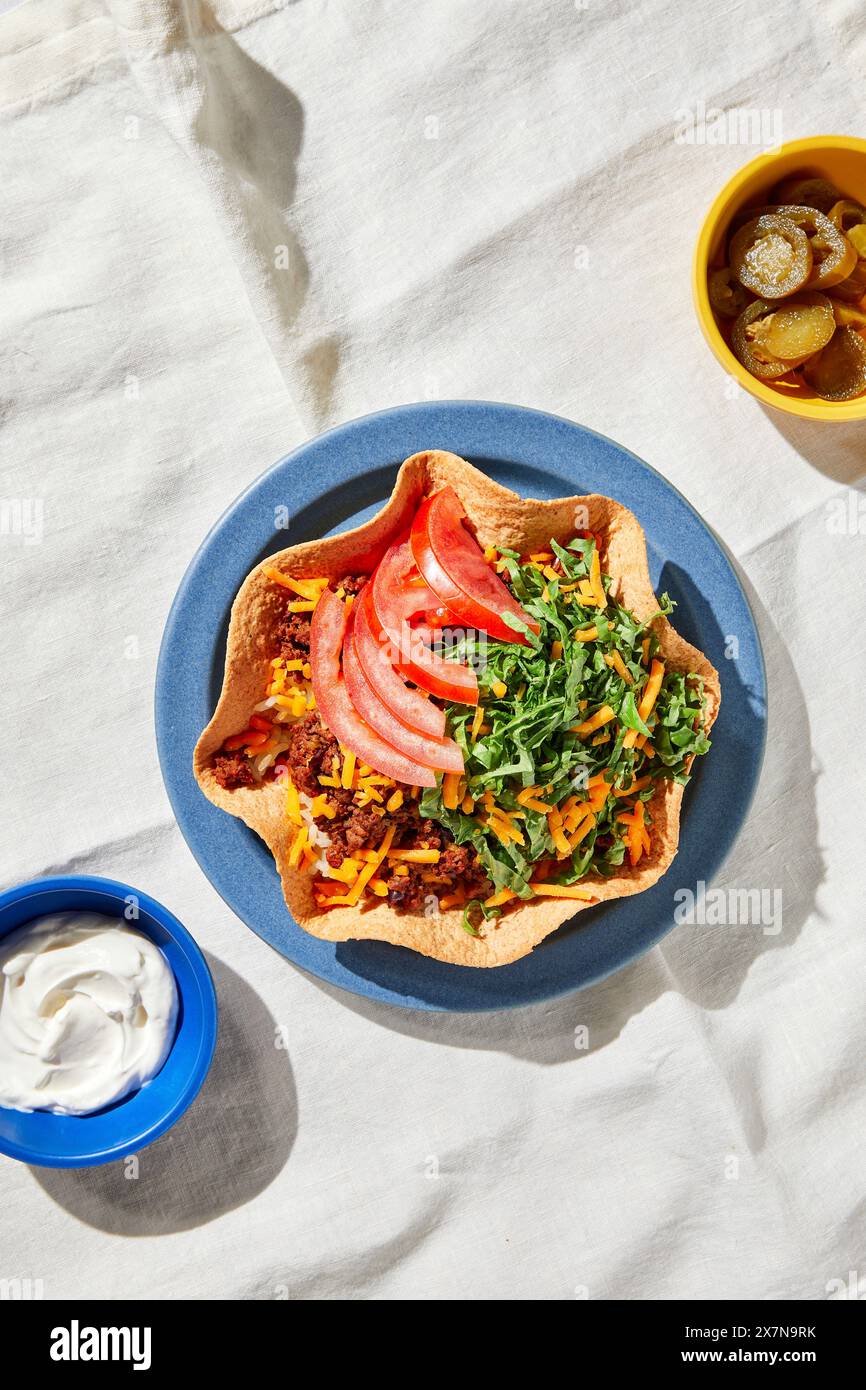 Bol à tacos de bœuf sur une assiette bleue et nappe blanche avec lumière dure Banque D'Images