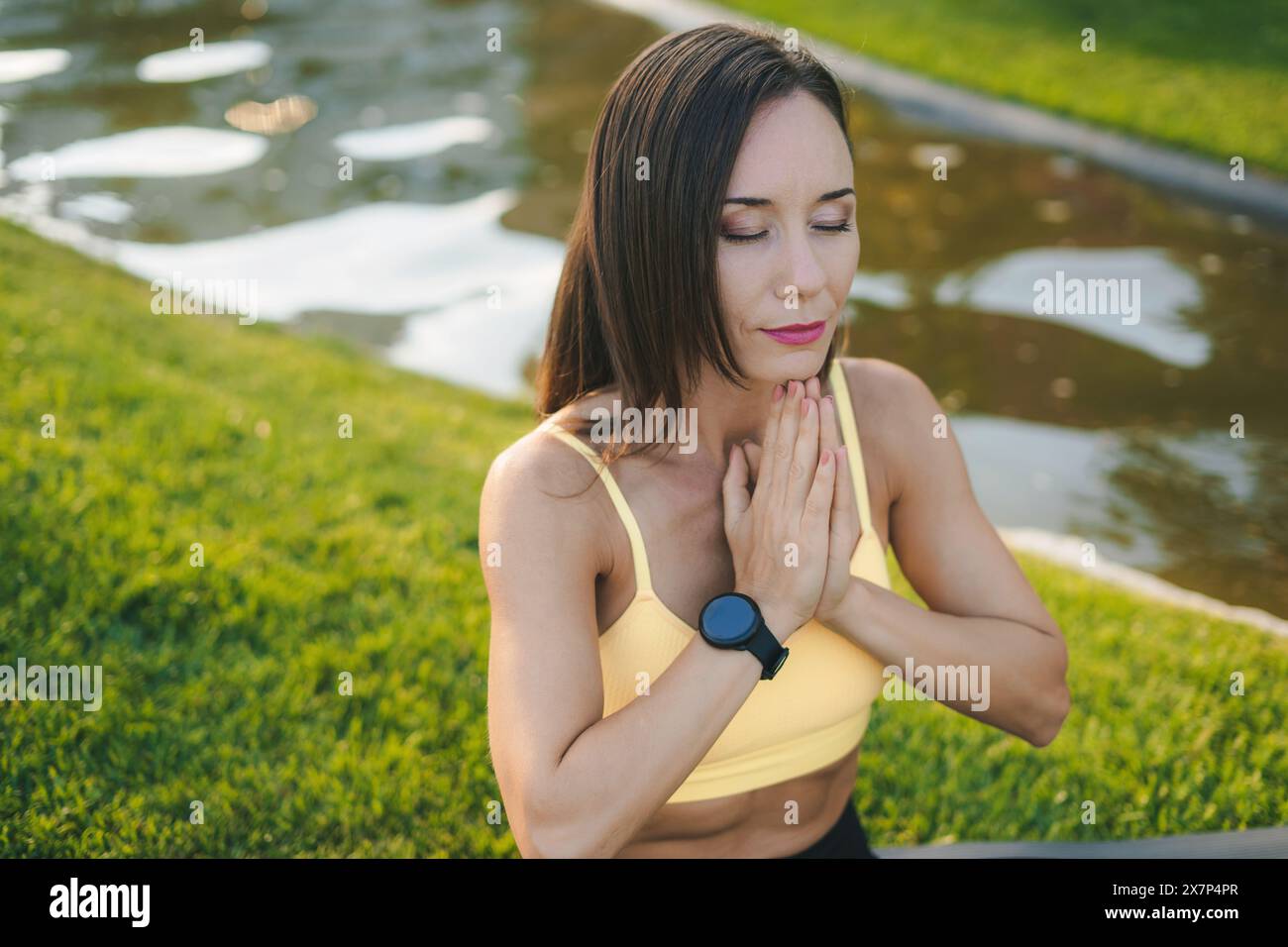 Femme adulte athlétique effectuant le yoga assis sur le tapis en position lotus à l'extérieur dans le parc de la ville. Femme sportive pendant la pratique de la méditation Banque D'Images