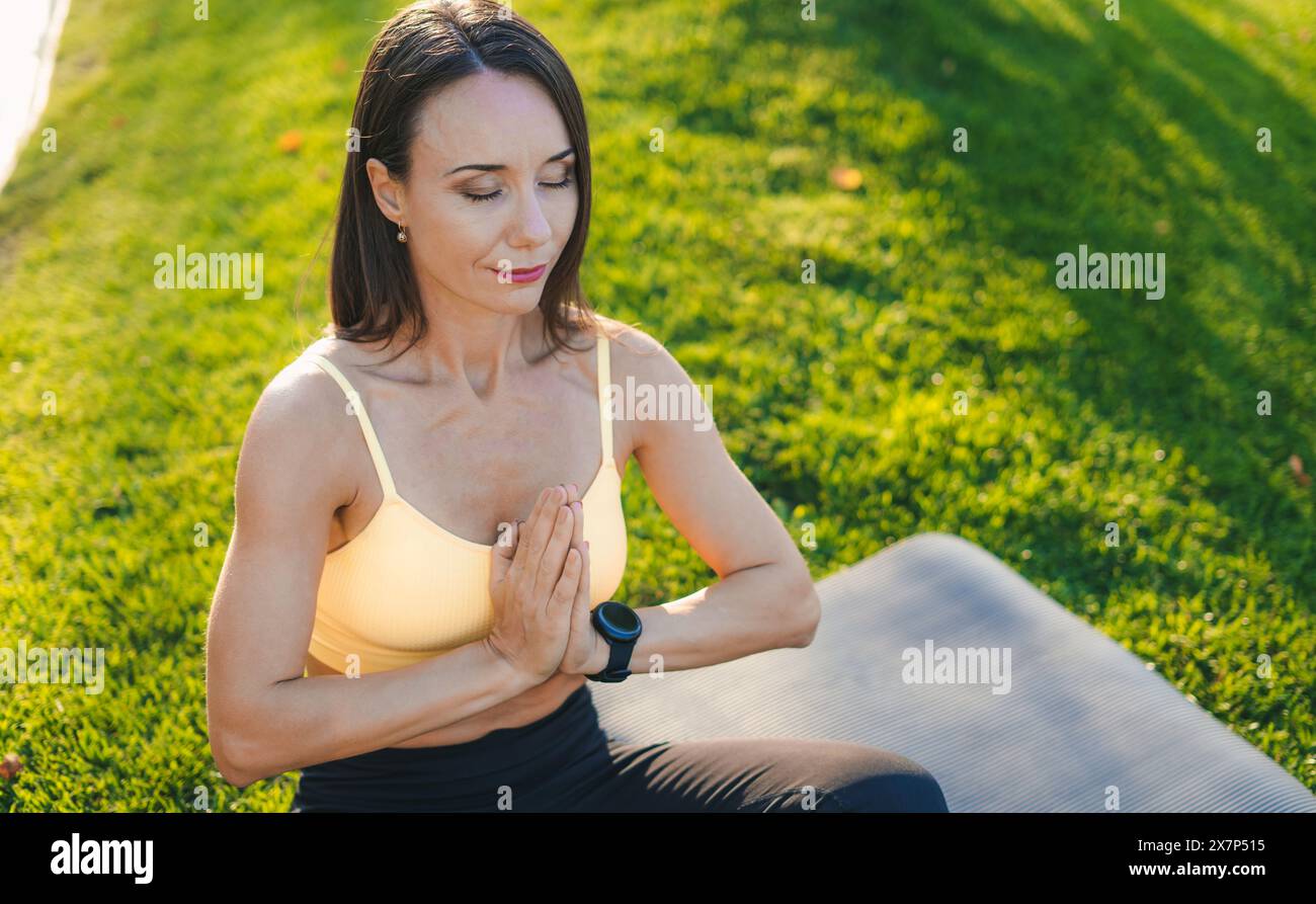 Femme dans le parc faisant du yoga, méditant sur un tapis de yoga, prenant soin de son corps et de sa santé mentale. Banque D'Images