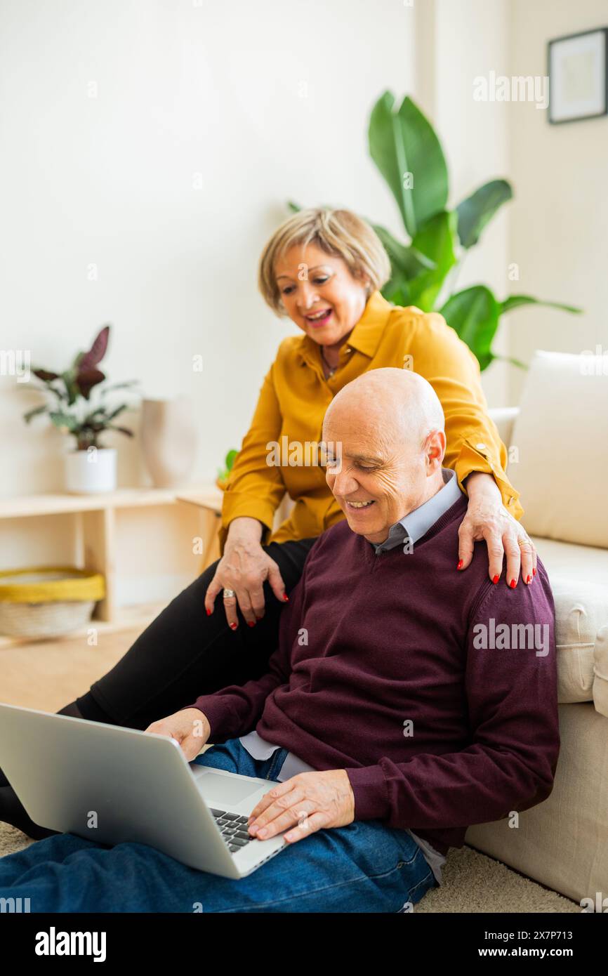 Couple senior ayant un appel vidéo sur un ordinateur portable, souriant à l'écran. Couple senior dans un salon, se connectant avec des proches en ligne. Banque D'Images