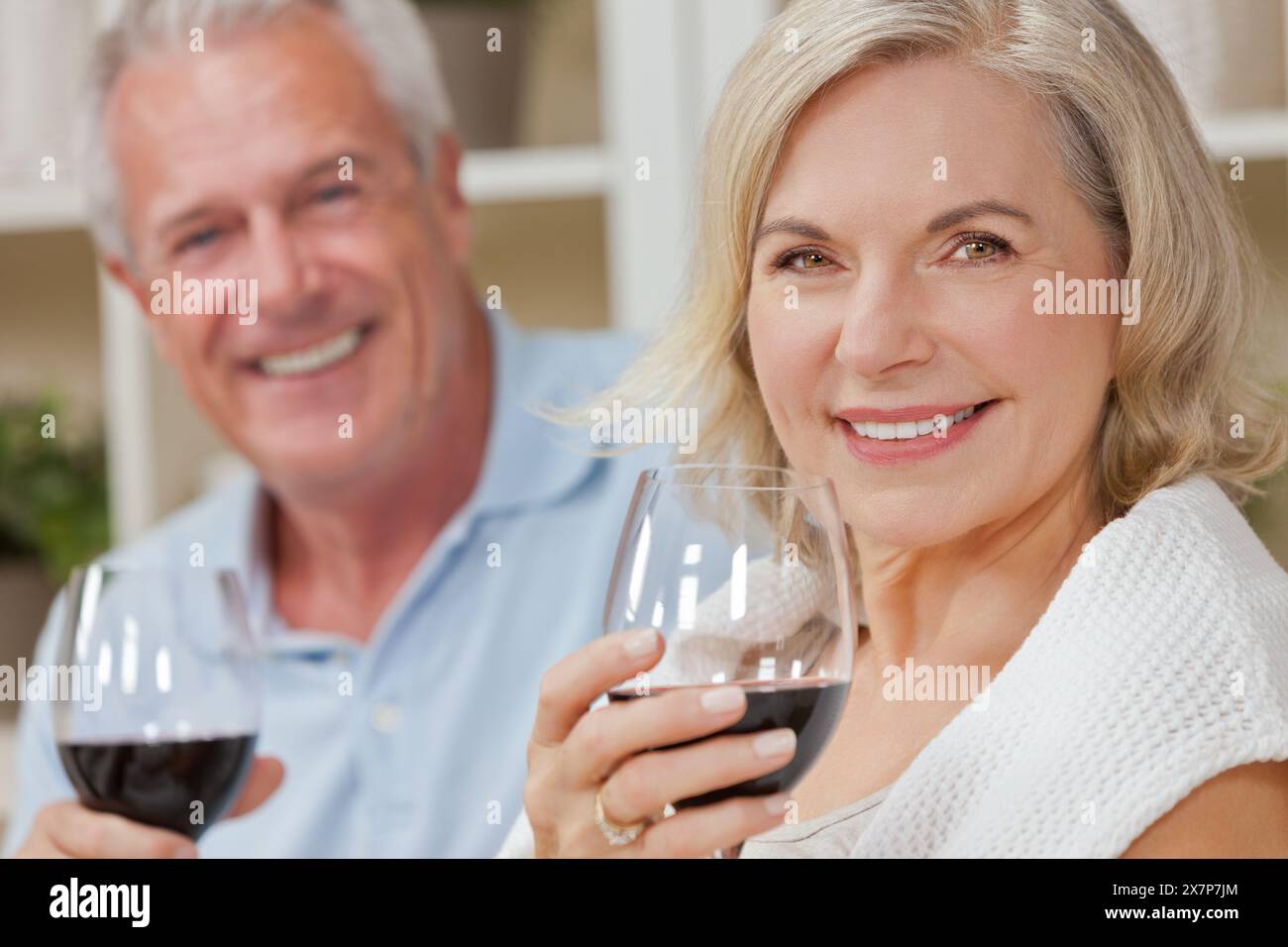 Happy senior man and woman couple assis ensemble à la maison de sourire et de boire du vin Banque D'Images