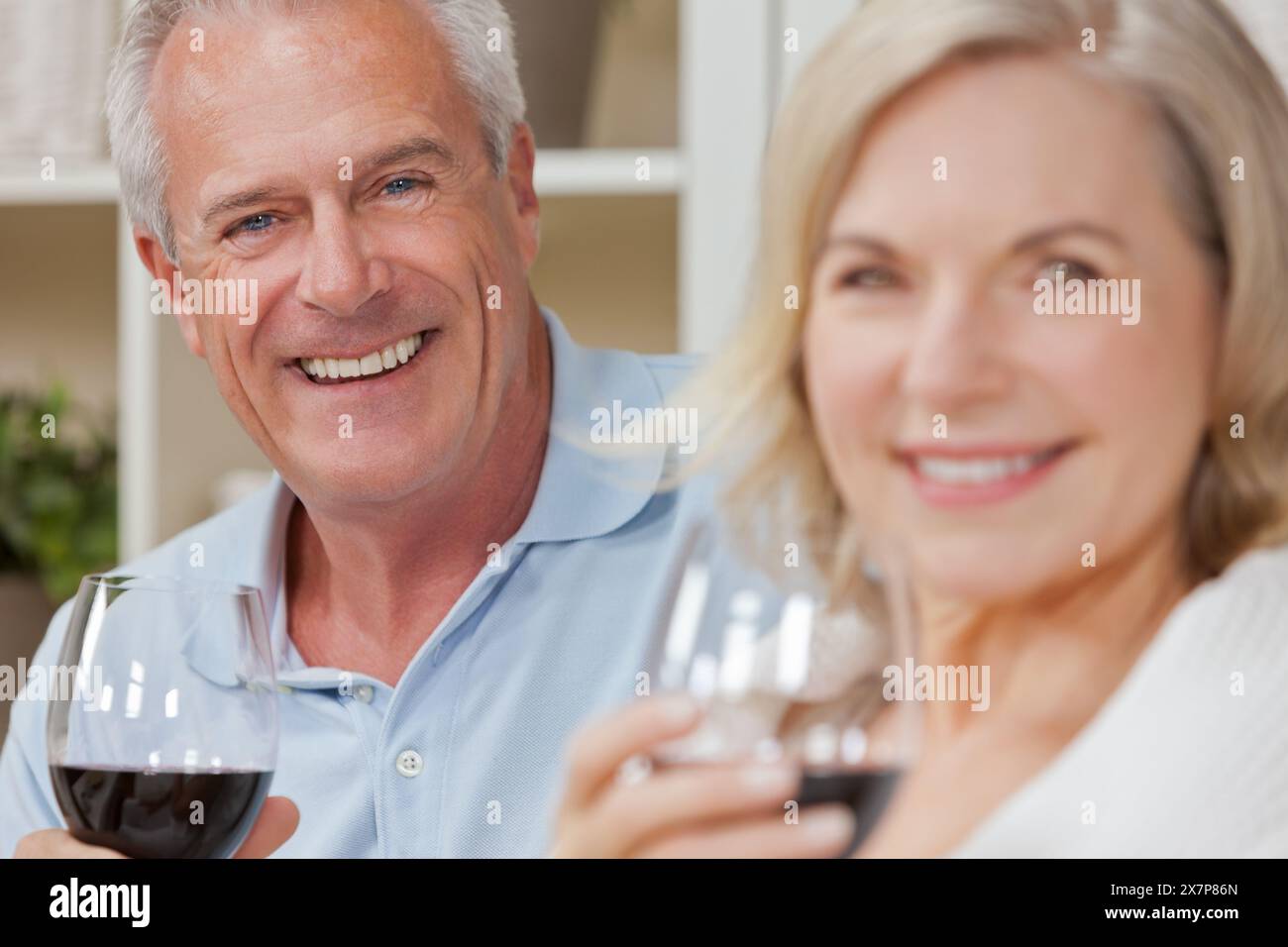 Happy senior man and woman couple assis ensemble à la maison de sourire et de boire du vin Banque D'Images