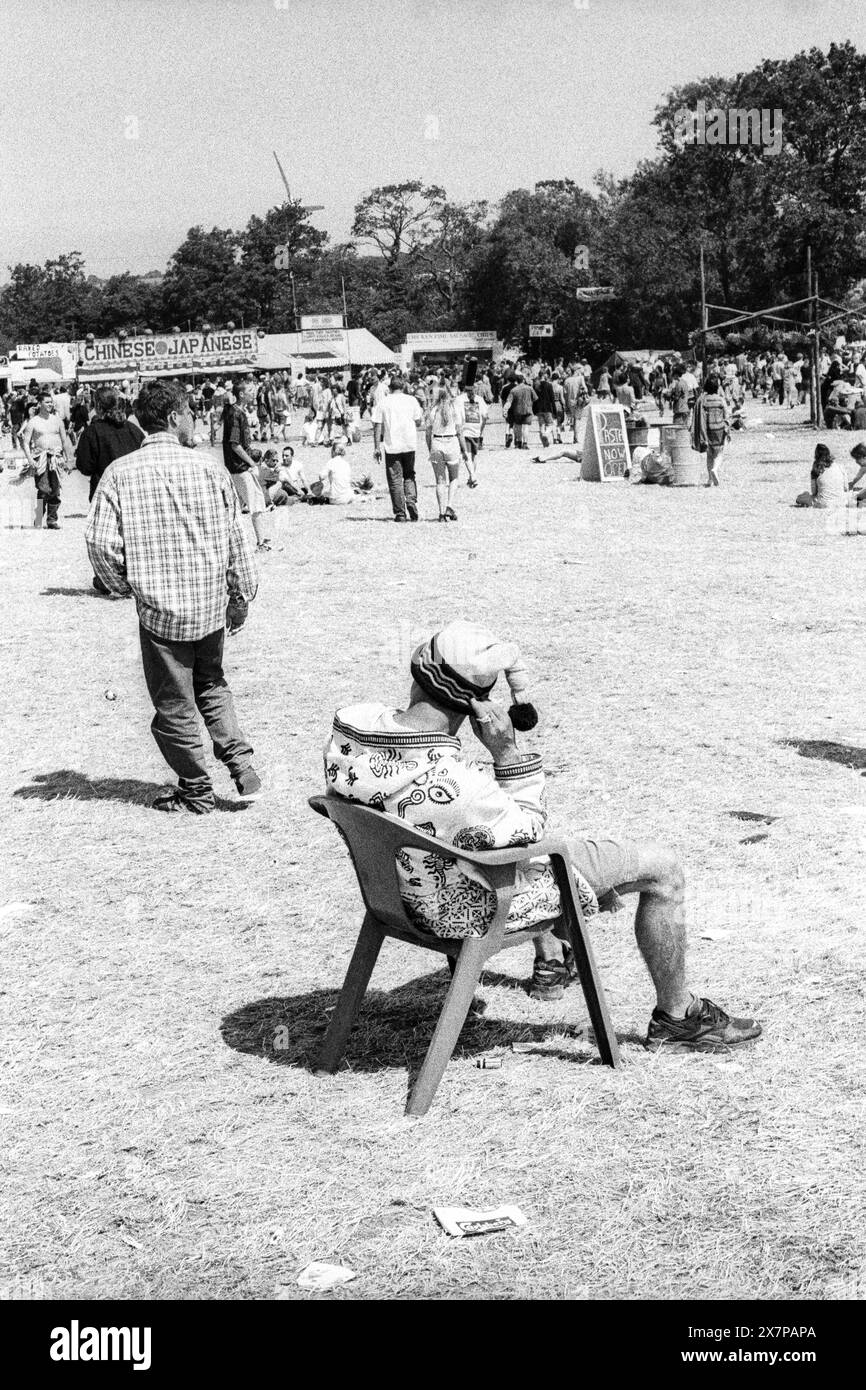 CROWD, HEATWAVE, NME STAGE, GLASTONBURY 95 : un homme repose sur une chaise en plastique dans un chapeau laineux sur l'herbe dans l'extrême canicule estivale près des stands de nourriture au Glastonbury Festival, Pilton Farm, Somerset, Angleterre, 24 juin 1995. En 1995, le festival a célébré son 25e anniversaire. Beaucoup de gens ont lutté avec un coup de chaleur lors du week-end particulièrement chaud. Photo : ROB WATKINS Banque D'Images