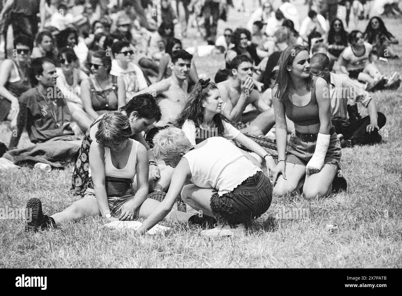 PROGRAMME DU FESTIVAL, CROWD, HEATWAVE, NME STAGE, GLASTONBURY 95 : les festivaliers s'écrasent sur l'herbe et vérifient la programmation du festival dans la vague de chaleur extrême de l'été au deuxième NME Stage Field et Crowd au Glastonbury Festival, Pilton Farm, Somerset, Angleterre, 24 juin 1995. En 1995, le festival a célébré son 25e anniversaire. Beaucoup de gens ont lutté avec un coup de chaleur lors du week-end particulièrement chaud. Photo : ROB WATKINS Banque D'Images