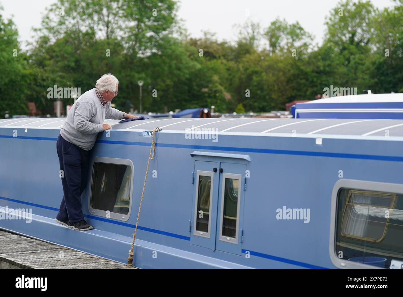 Un homme nettoie un bateau sur le canal, à Crick Marina à Crick, Northamptonshire, avant le Crick Boat Show pendant le week-end des vacances bancaires. Date de la photo : mardi 21 mai 2024. Banque D'Images