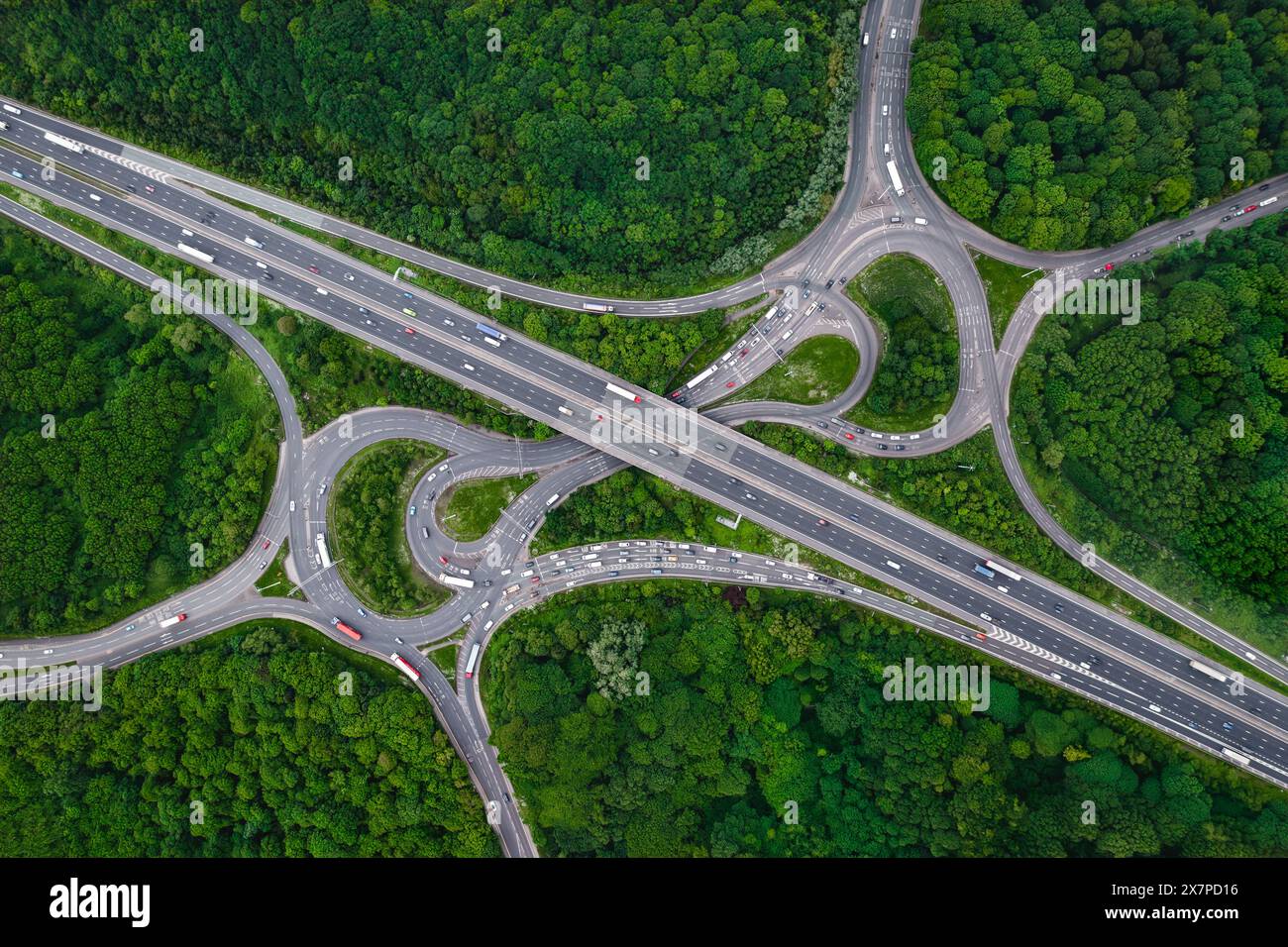 Vue aérienne du paysage directement au-dessus d'une jonction d'autoroute très fréquentée coupant un andain à travers une forêt dense avec une canopée verte d'arbres fournissant la capture de carbone Banque D'Images